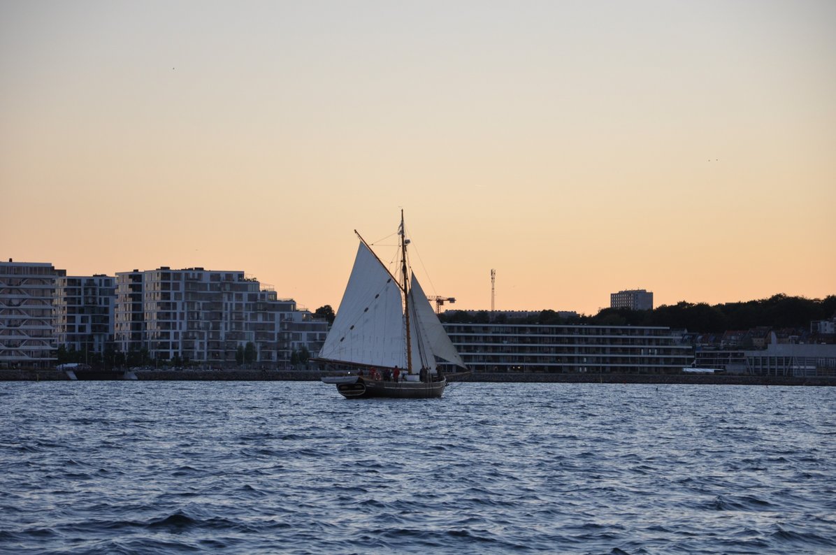 A sailing boat by a sunset on an ocean by the harbour
