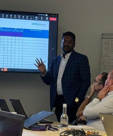 Man wearing a suit. standing in front of a screen presenting to his colleagues